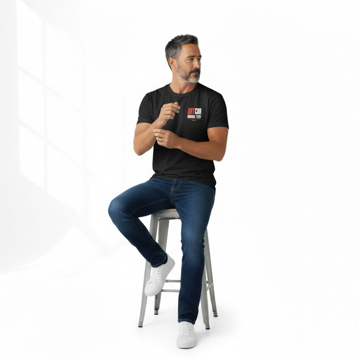 A second model seated on a stool wearing the black KCAM Art Car tee, front view, with the ARTCAR MANUAL TECH print on the left chest